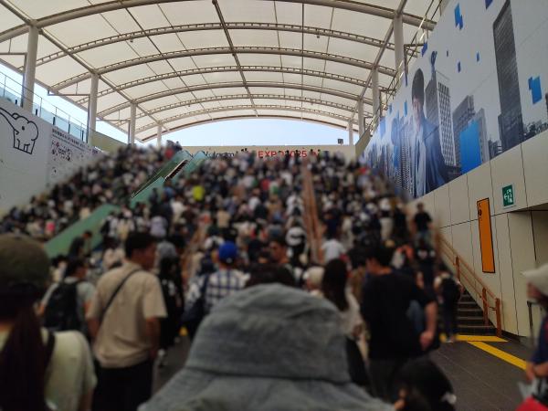 ドーム状の屋根の下、夢洲駅から万博会場へ向かう人々で混み合う階段とエスカレーター。