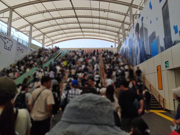 ドーム状の屋根の下、夢洲駅から万博会場へ向かう人々で混み合う階段とエスカレーター。