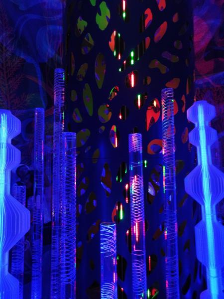 青い光に満たされた空間で、豹柄の穴あき装飾柱と、らせん状に光る透明な円柱が並ぶ幻想的な展示。