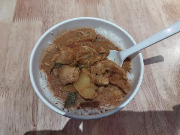 使い捨て容器に入った、茶色いルーと鶏肉が乗ったカレーライス。白いスプーンが添えられています。