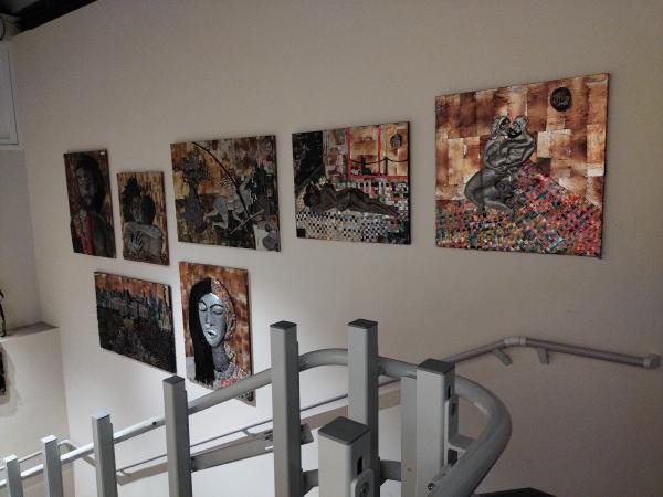 階段の横の壁に、暗いトーンで描かれた人物や抽象的な模様の絵画が7点展示されています。