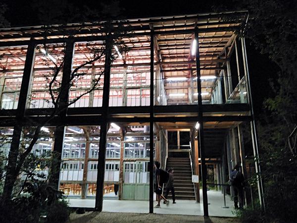 夜間、明るく照明が灯された、ガラスと木材でできた2階建ての建物の入り口付近。
