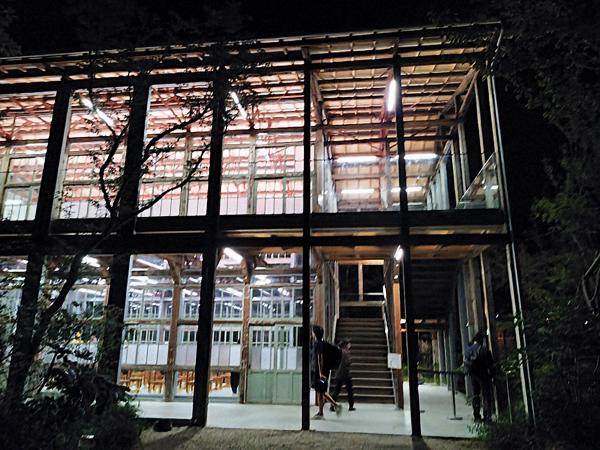 夜間、明るく照明が灯された、ガラスと木材でできた2階建ての建物の入り口付近。