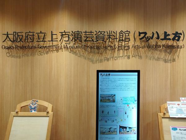 「大阪府立上方演芸資料館（ワッハ上方）」の木目調の壁の看板と展示の説明。