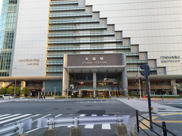 JR大阪駅の正面入り口を写しています。「OSAKA STATION」の大きな看板が目立ち、上部には階段状のガラス窓を持つモダンな駅ビルがそびえ立っています。