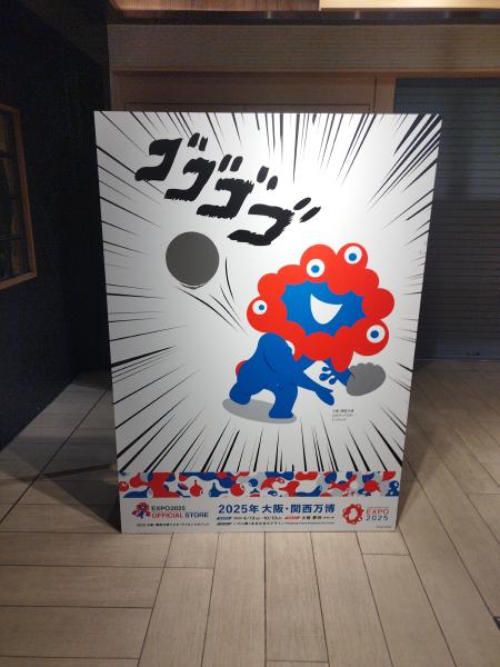 大阪・関西万博の公式キャラクター「ミャクミャク」の顔はめパネルです。赤と青の奇抜なデザインのキャラクターと共に、漫画的な「ゴゴゴゴ」の文字が描かれ、万博開催への期待感を高める展示物です。