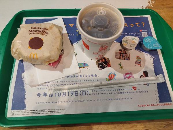 マクドナルドで提供された朝食セットです。紙に包まれたソーセージマフィンとプレミアムローストアイスコーヒーのドリンクカップが緑色のトレイに載っています。