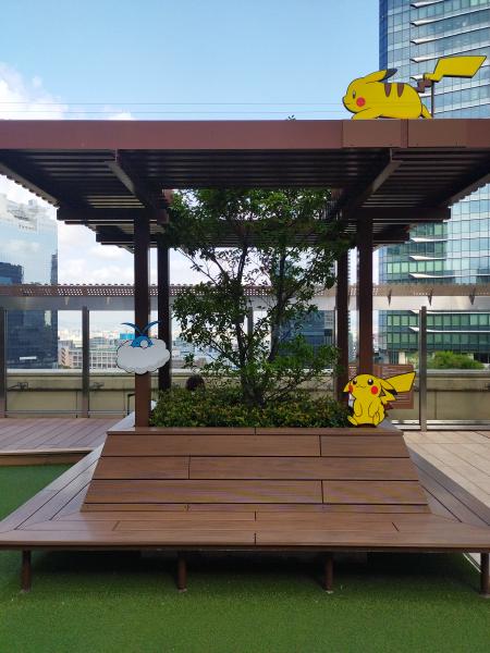 建物の屋外広場にある、木製のパーゴラと植え込み、そして楽しそうなピカチュウとチルタリスのキャラクターボードが飾られています。