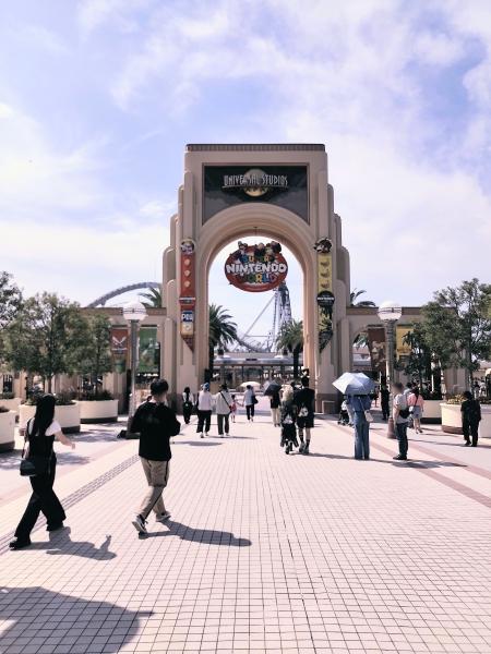 青空の下、ユニバーサル・スタジオ・ジャパンのエントランスアーチをくぐる多くの来場者。