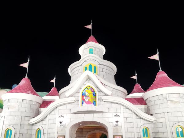 夜間のスーパー・ニンテンドー・ワールド。中央にマリオの世界を模した立体的なエリア、左にクッパ城の要塞。